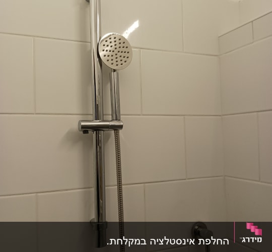 ראש מקלחת מתכת על קיר אריחים לבנים